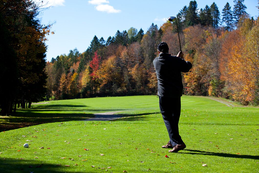 Golfer swings club in autumn