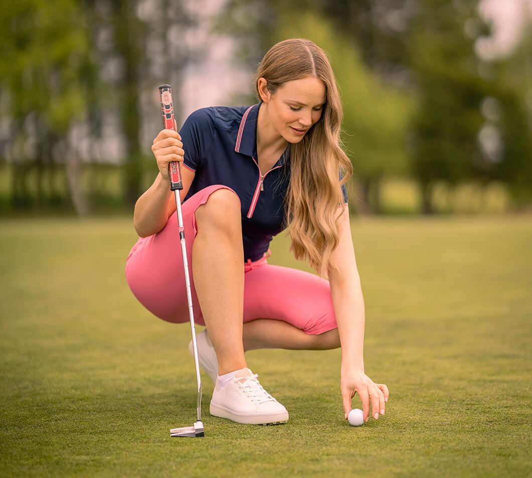 Woman lining up golf shot in polo shirt and golf trousers