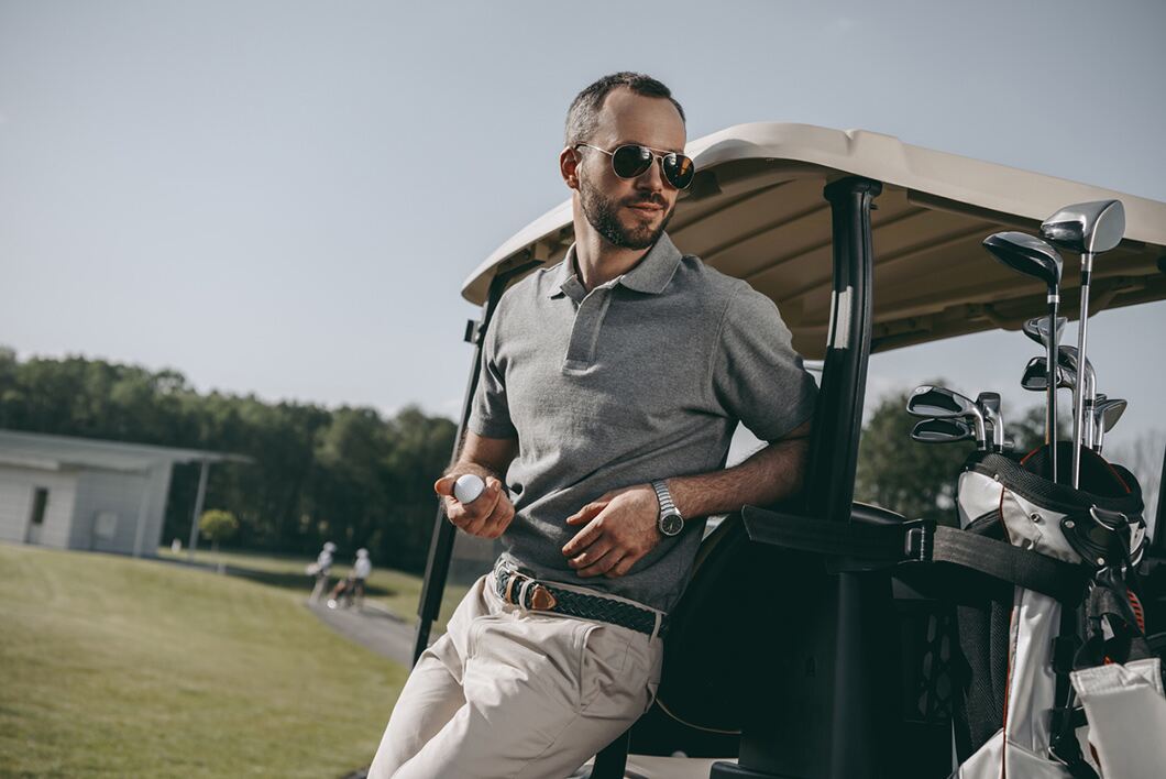 Man leans against golf buggy in stylish clothes