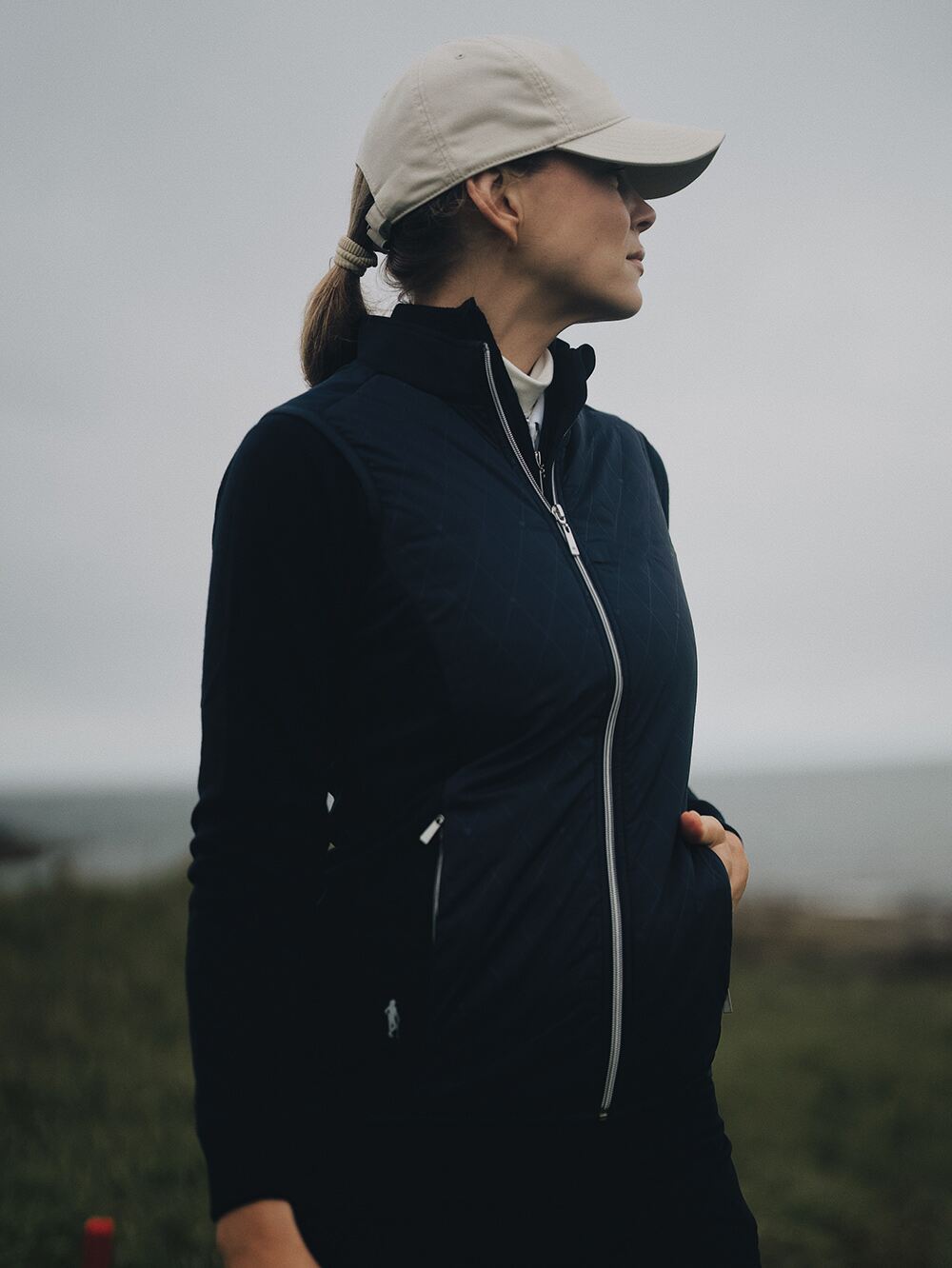 A woman on a golf course in a navy golf gilet and beige cap